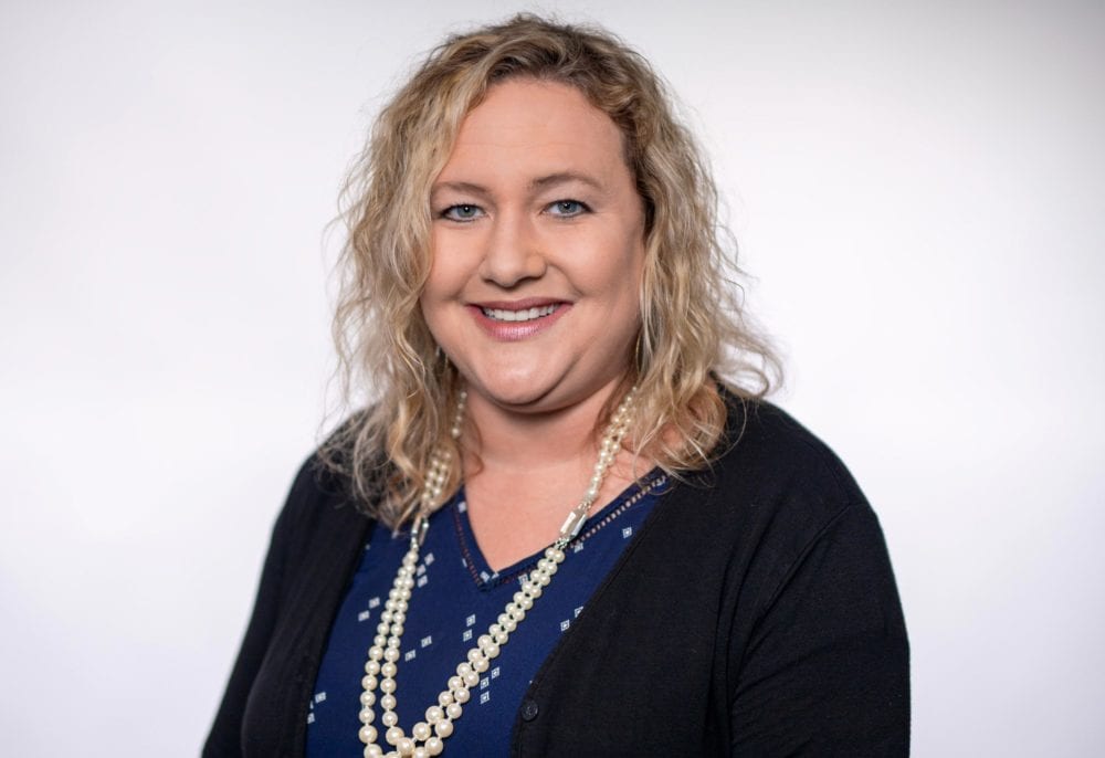 A headshot of Alice Keener—a white woman with blonde hair, wearing a black cardigan over a blue shirt.