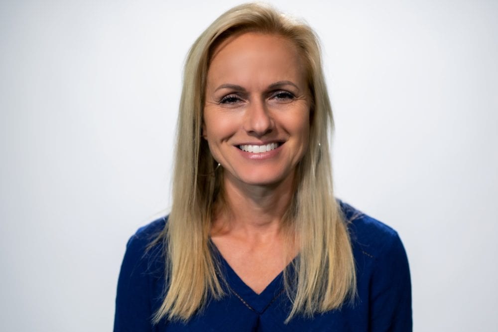 A headshot of Ayisha Canant—a white woman with long blonde hair, wearing a blue blouse.