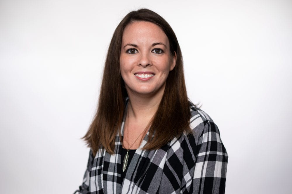 A headshot of Chelsea Farrar—a white woman with long brown hair, wearing a black and white plaid shirt.