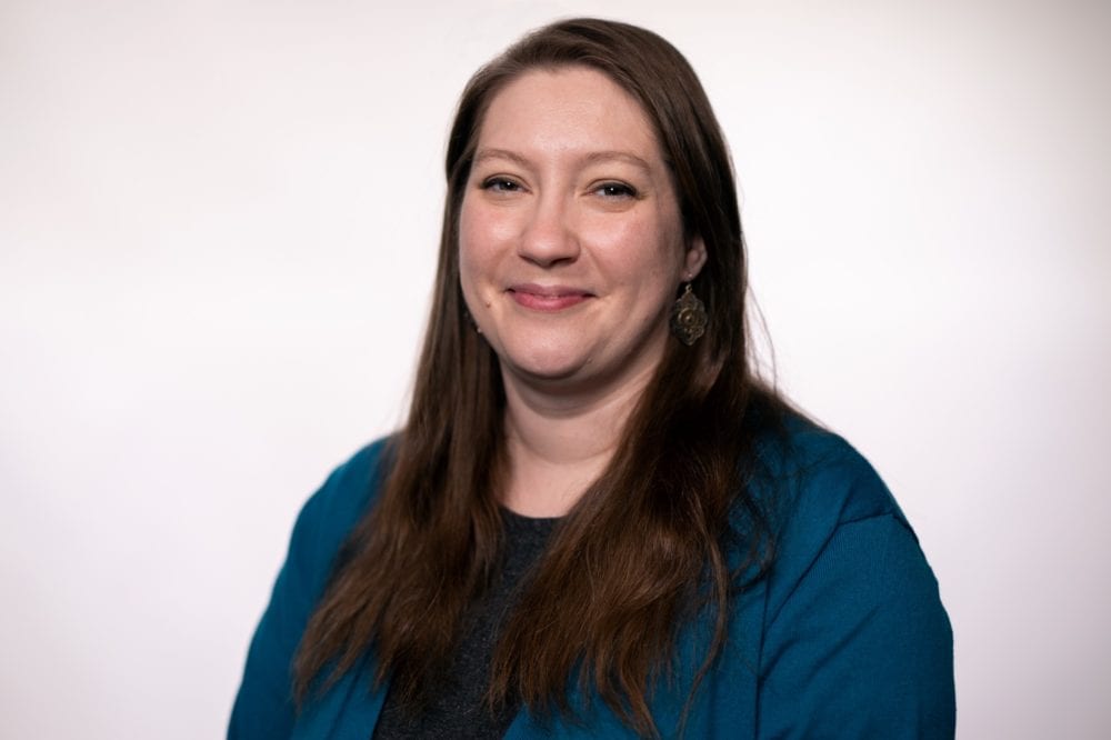 A headshot of CariAnn Bergner-Moore—a white woman with long brown hair and a navy cardigan.
