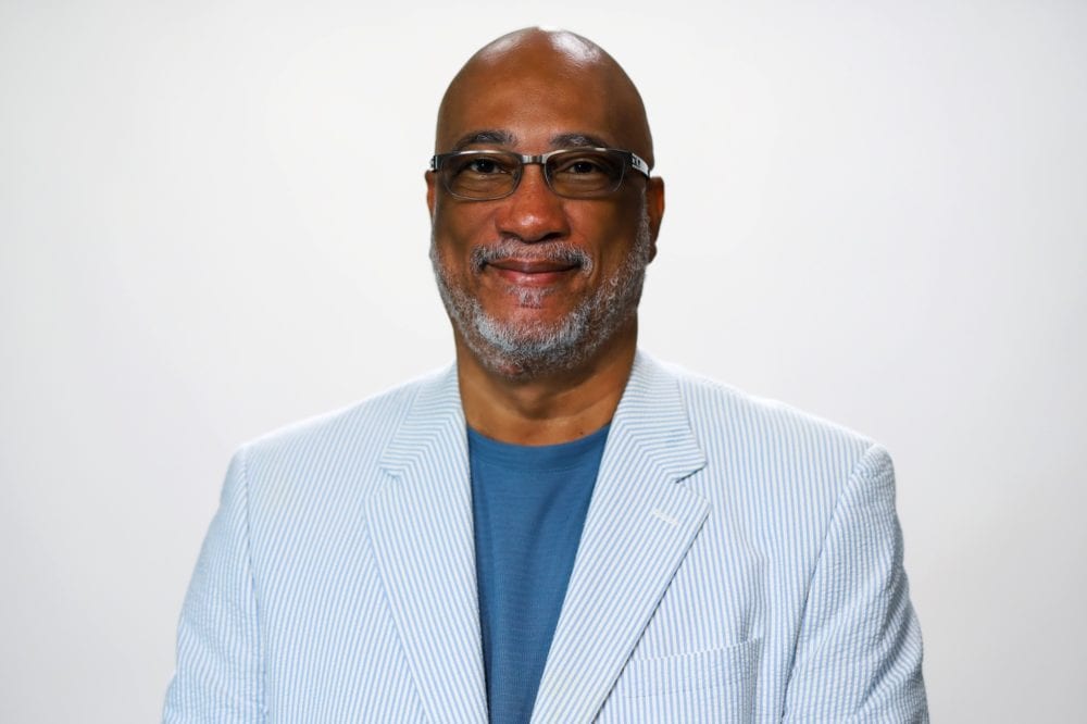 A headshot of John Knott—a bald black man wearing a light blue pinstriped jacket.