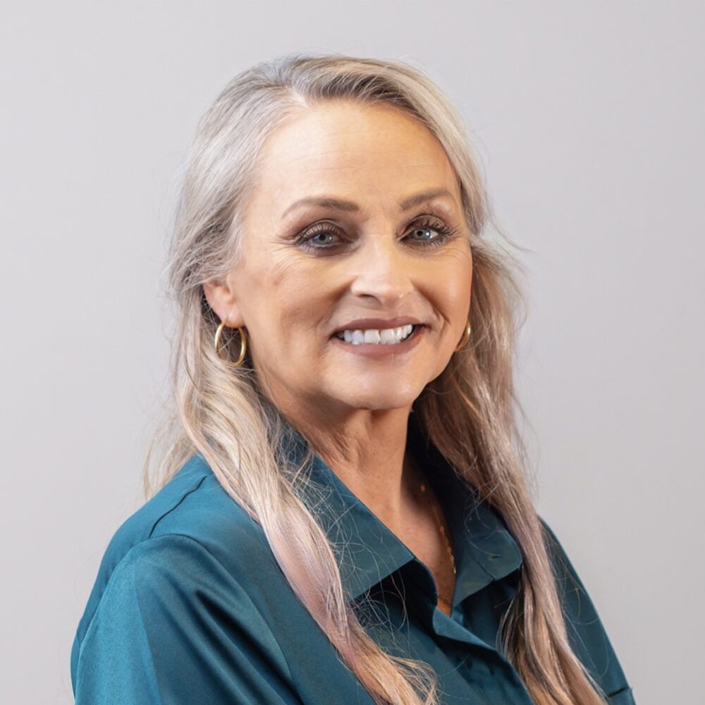 A headshot of Monica Roberts—an older woman with blonde hair, wearing a green-blue button up.