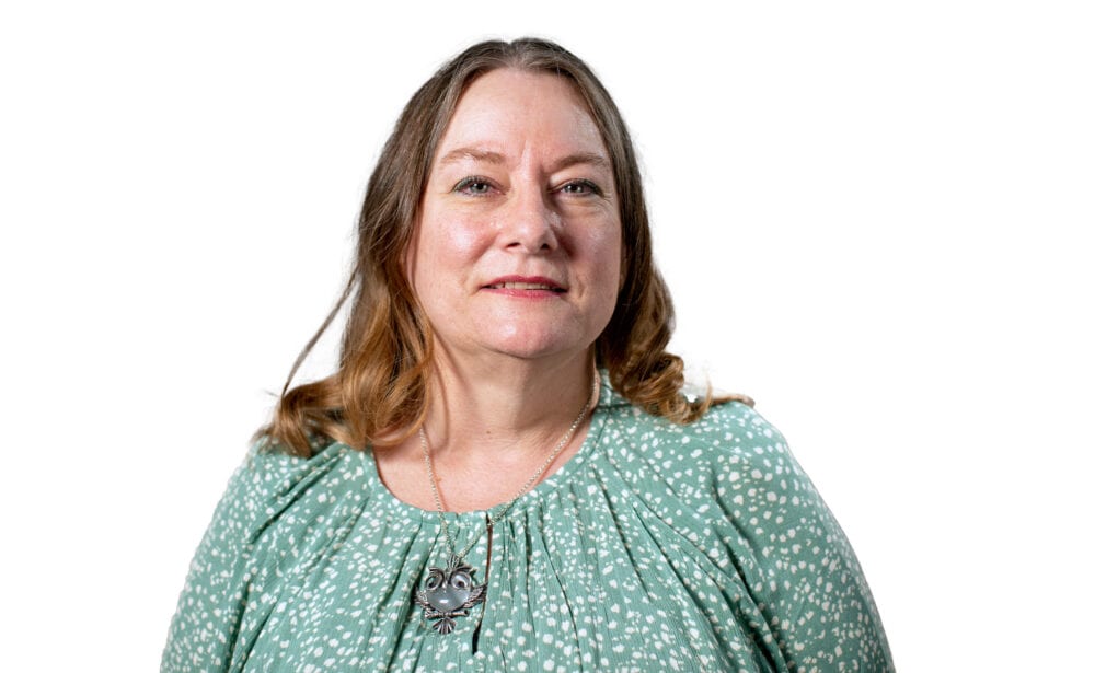 A headshot of Teresa Belknap—a middle-aged white woman with shoulder-length brown hair, wearing a green shirt with white polkadots