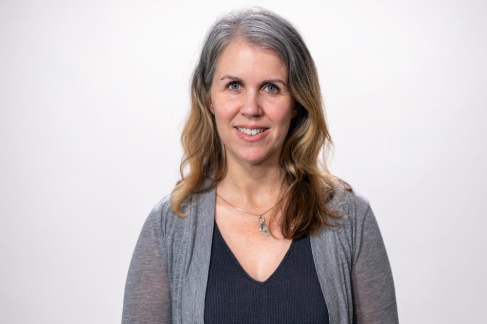 Headshot of Tracie Wells—a middle-aged white woman with gray and brown hair, wearing a black shirt and gray cardigan.