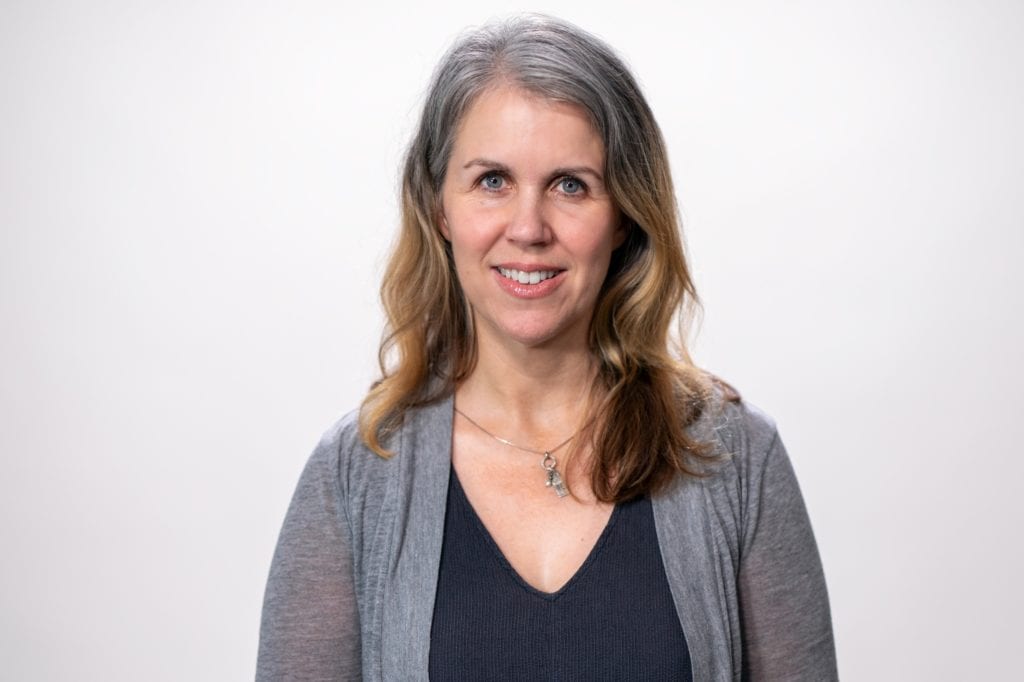 Headshot of Tracie Wells—a middle-aged white woman with gray and brown hair, wearing a black shirt and gray cardigan.