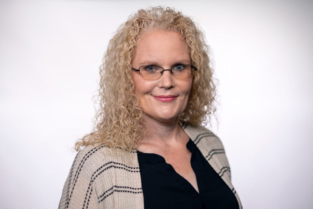 A headshot of Amber Mckenzie—an older woman with curly blonde hair and a tan cardigan.