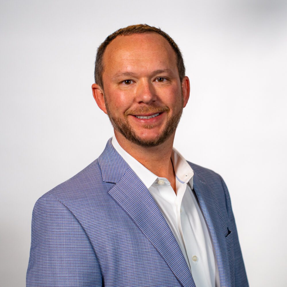 A headshot of James McCormack—a middle-aged man with short brown hair and a beard. He is wearing a blue small plaid suit jacket and white shirt.