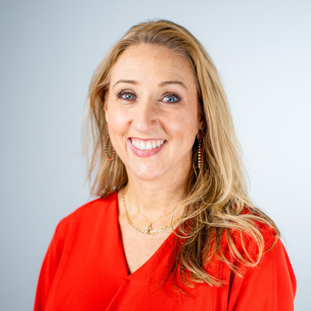 A headshot of Angela Holyfield—a blonde middle-aged woman wearing a bright red blouse.