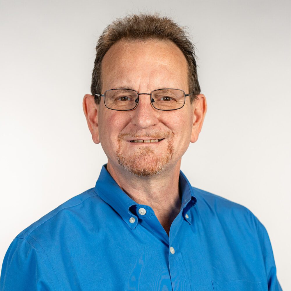 A headshot of David Hawkins—an older man with brown hair and a goatee wearing a blue button up shirt.